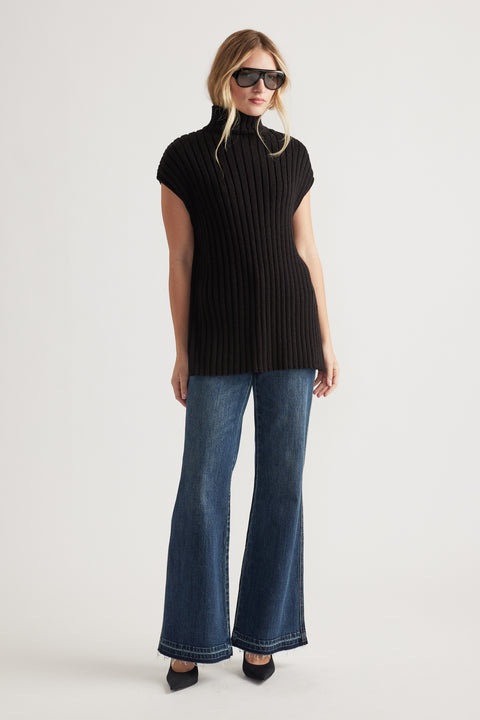 Woman wearing a black ribbed high-neck knit tunic styled with wide-leg denim jeans and black pointed-toe shoes
