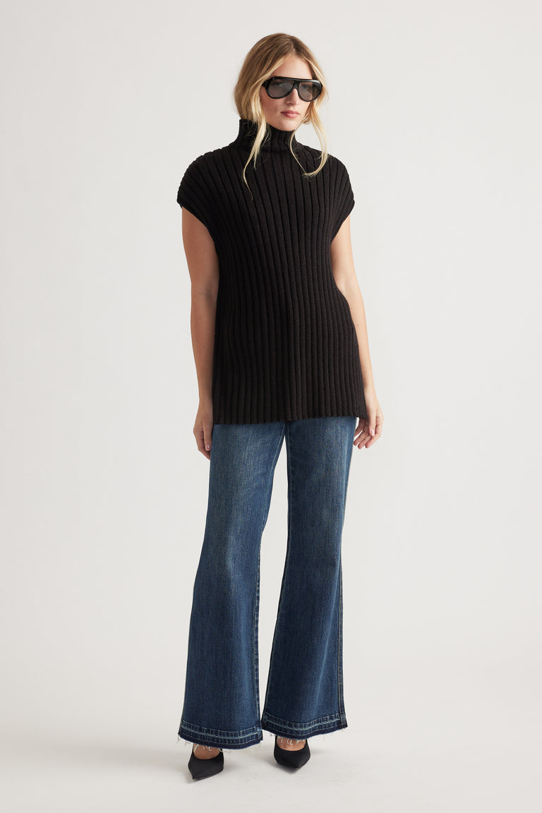 Woman wearing a black ribbed high-neck knit tunic styled with wide-leg denim jeans and black pointed-toe shoes