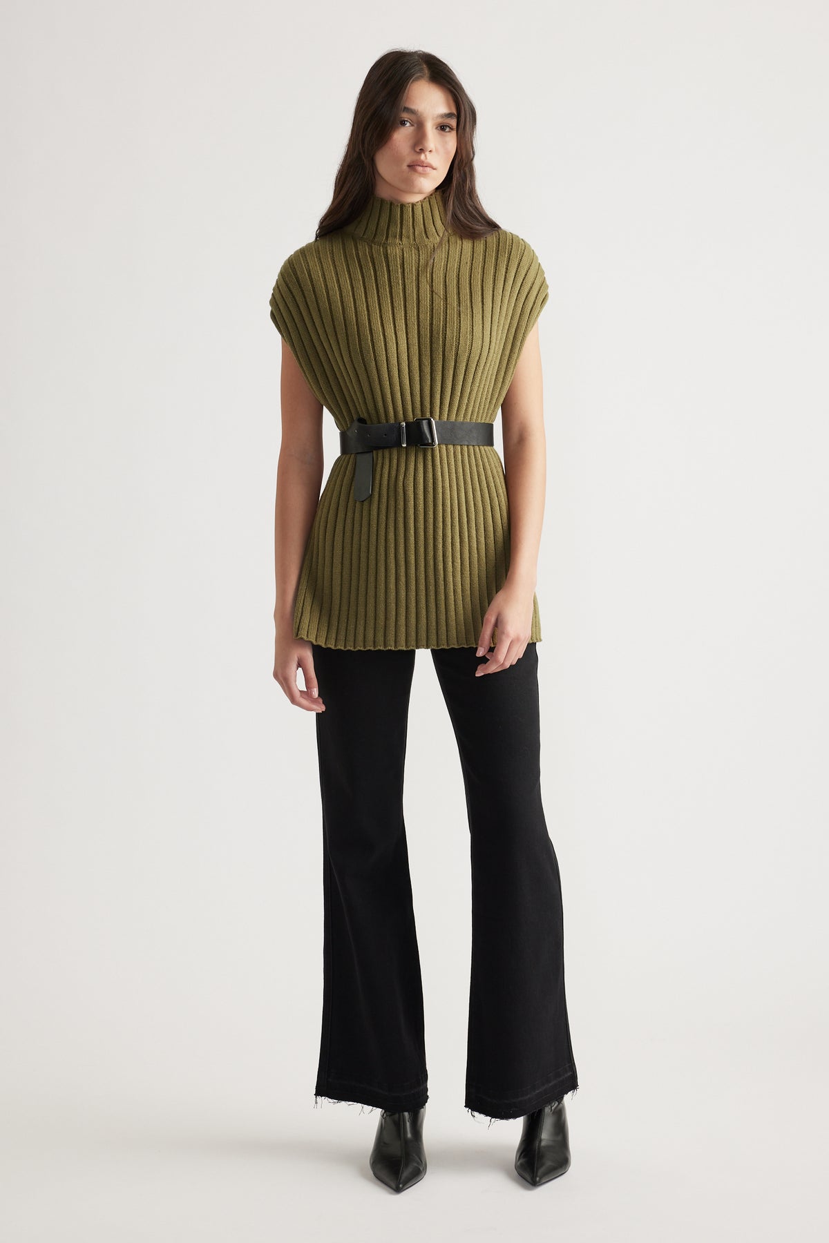 Woman wearing an olive high-neck ribbed knit tunic with a black belt, paired with flared black jeans and black boots