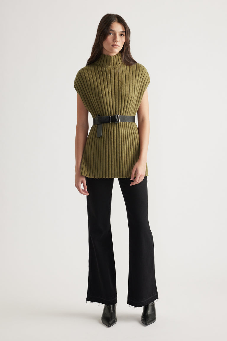 Woman wearing an olive high-neck ribbed knit tunic with a black belt, paired with flared black jeans and black boots