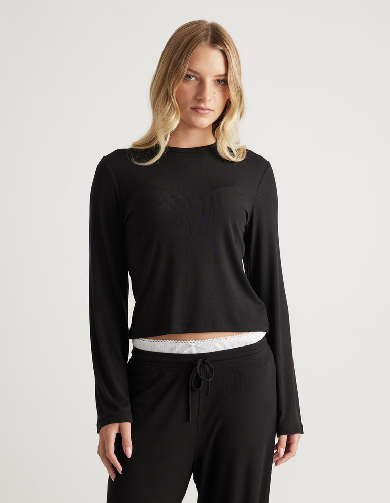 Woman wearing a fitted black ribbed long sleeve top paired with matching black drawstring pants for cozy loungewear style