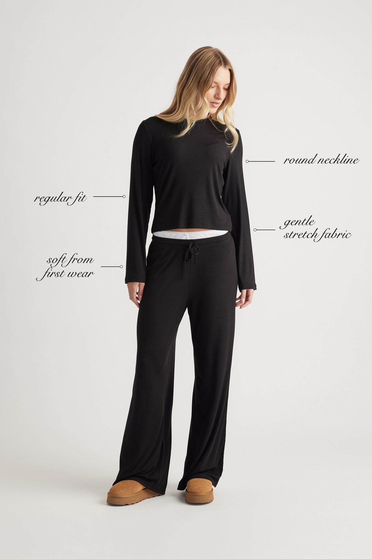 Woman wearing a black ribbed long sleeve top with round neckline and relaxed fit paired with wide leg pants and slippers