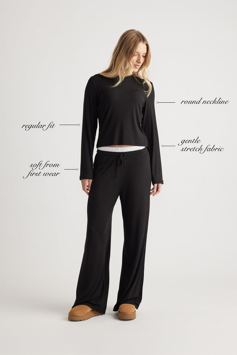 Woman wearing a black ribbed long sleeve top with round neckline and relaxed fit paired with wide leg pants and slippers