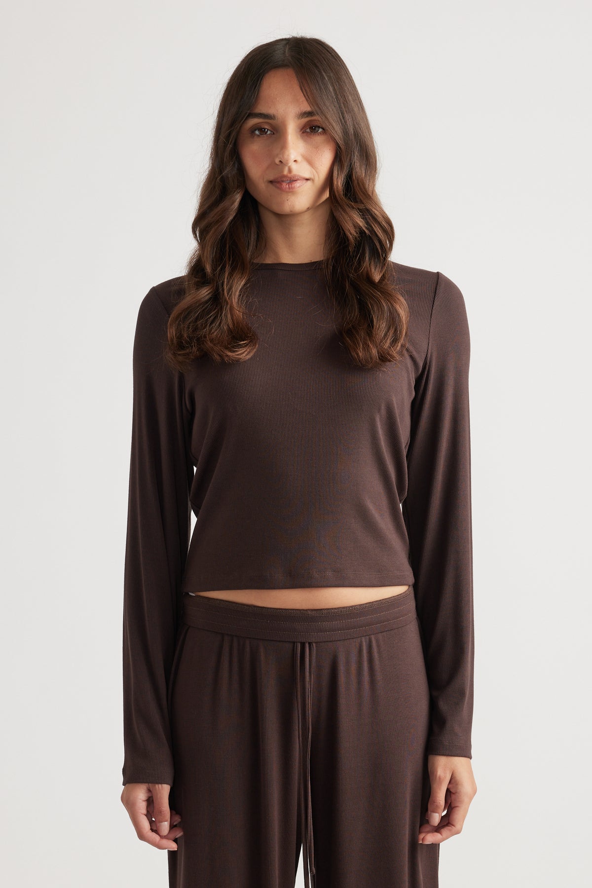 Woman modeling a dark brown ribbed long sleeve top with relaxed fit and matching wide-leg lounge pants