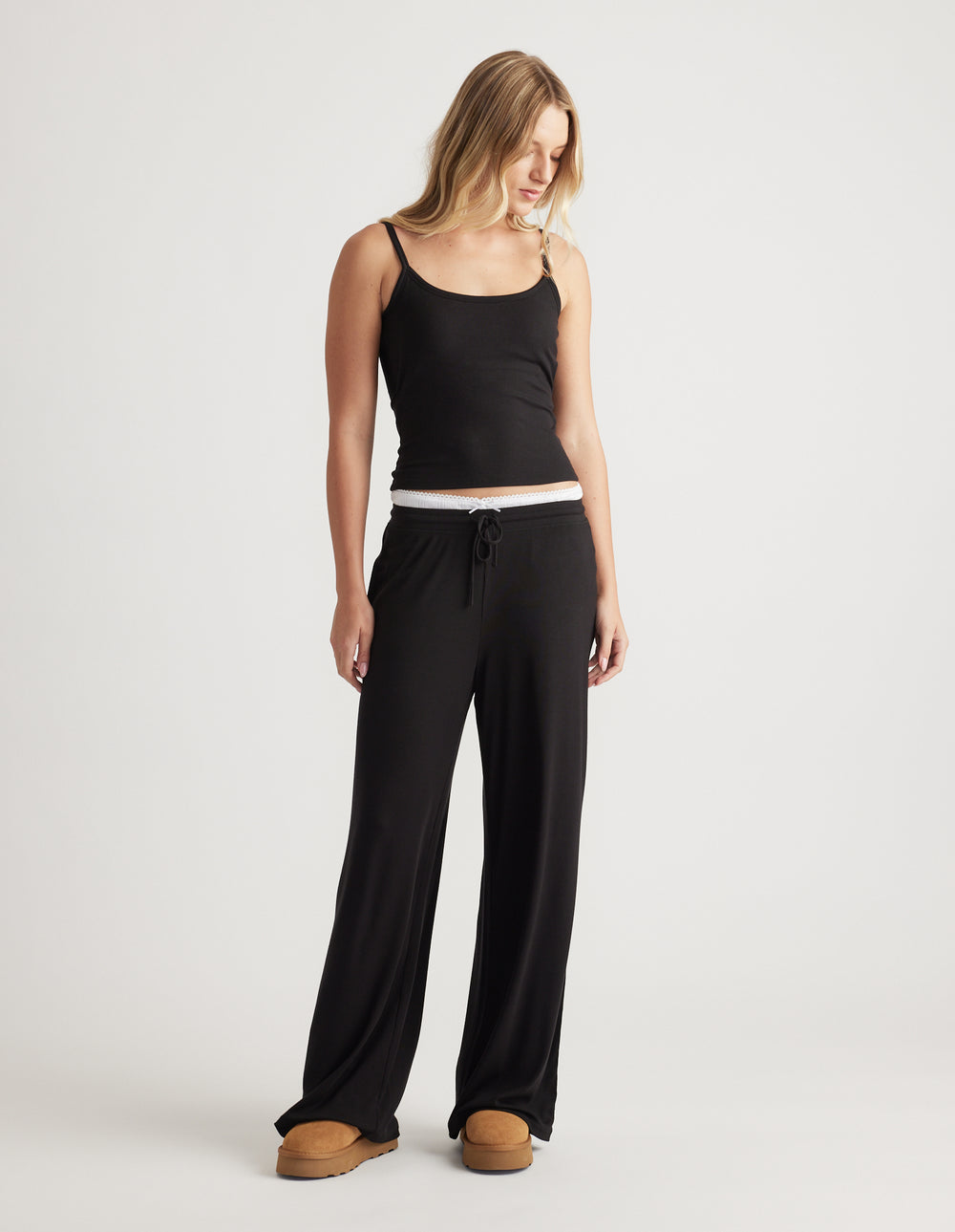 Woman wearing relaxed black ribbed wide leg pants with drawstring waist and a fitted black cami top for casual comfort