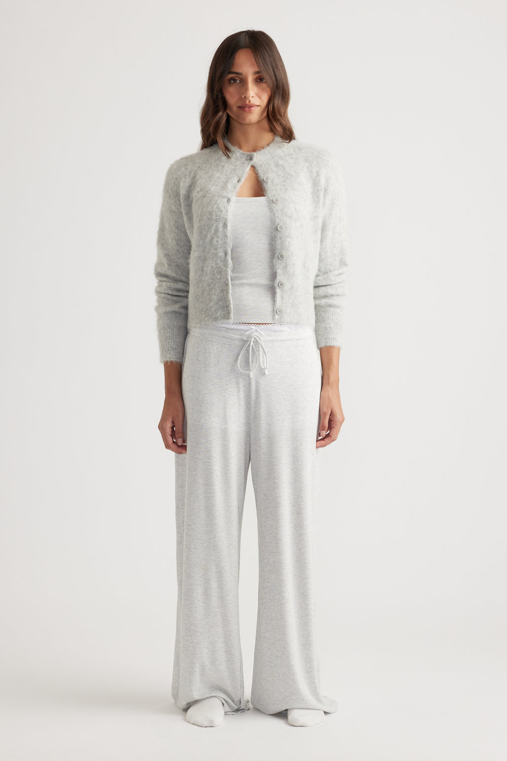 Woman wearing soft light grey wide leg pants with drawstring waist paired with a cozy button-up cardigan and tank top