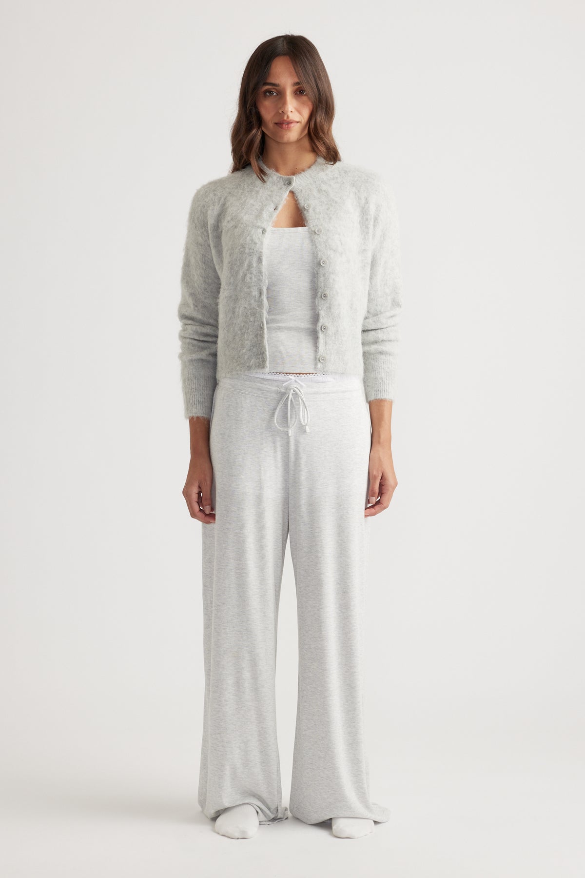 Woman wearing soft light grey wide leg pants with drawstring waist paired with a cozy button-up cardigan and tank top