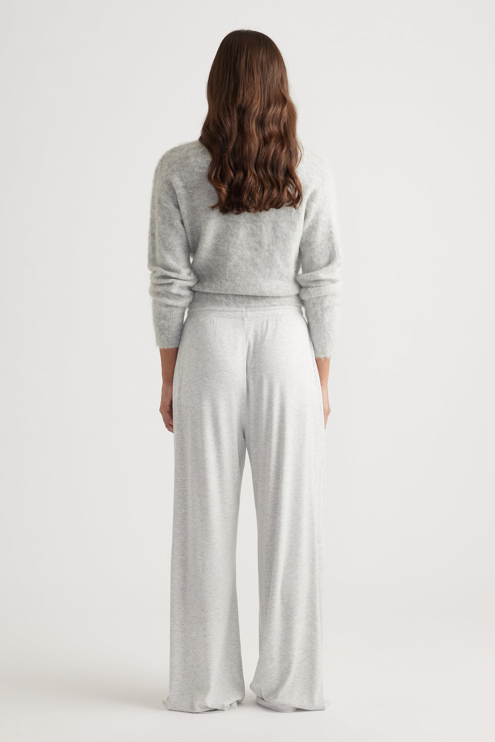 Woman wearing soft light grey ribbed wide leg pants paired with a cozy fuzzy knit sweater from the back view