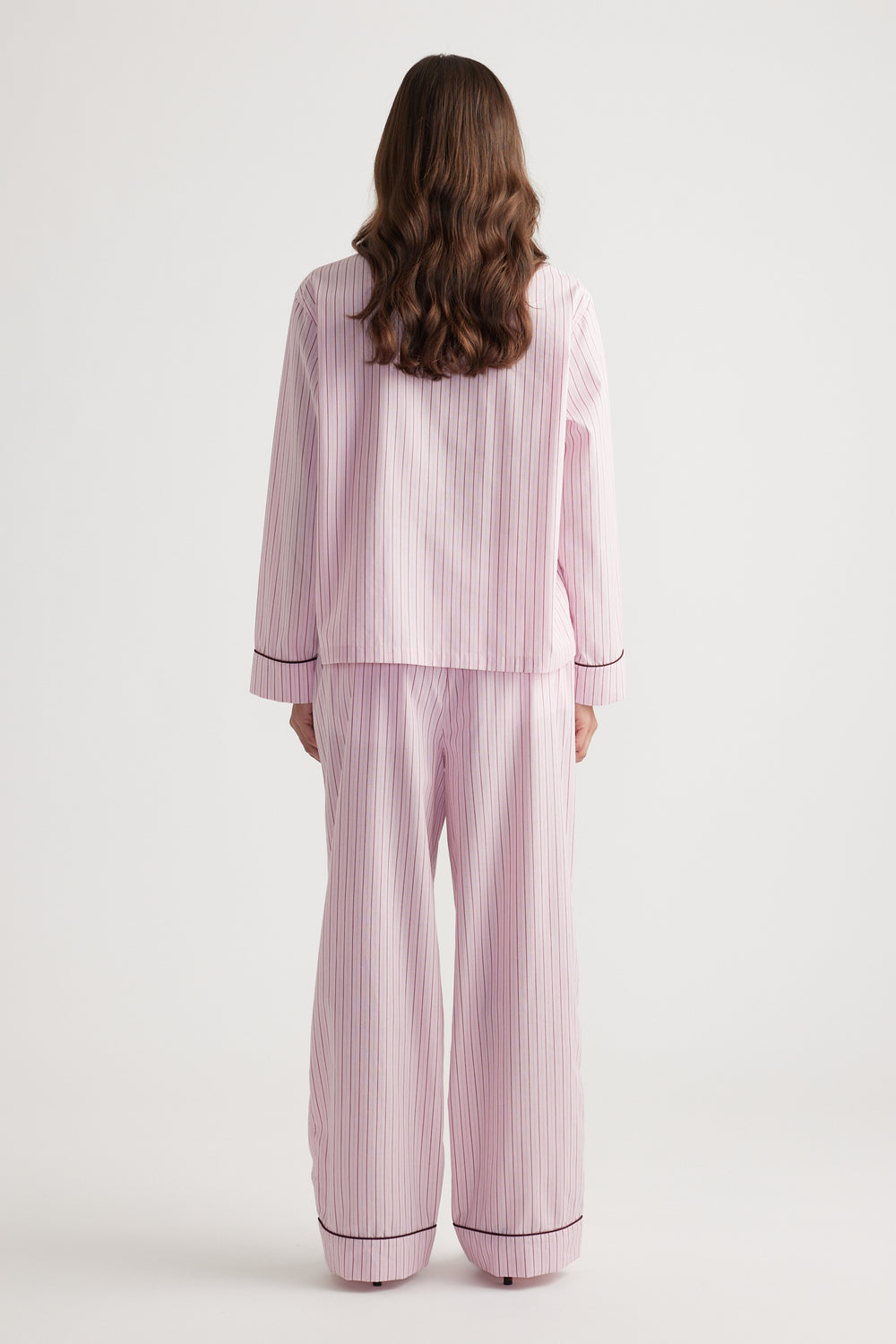 Woman shown from behind wearing soft pink striped wide leg sleep pants and matching long sleeve top with contrast trim