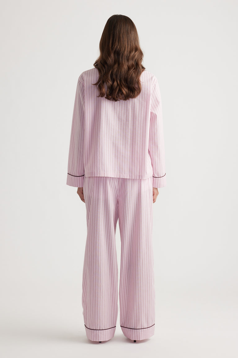 Woman shown from behind wearing soft pink striped wide leg sleep pants and matching long sleeve top with contrast trim