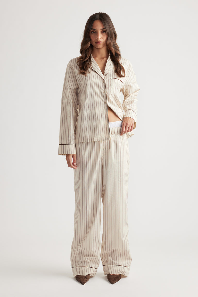 Woman wearing cream striped woven long sleeve shirt and matching wide-leg pants standing against white background