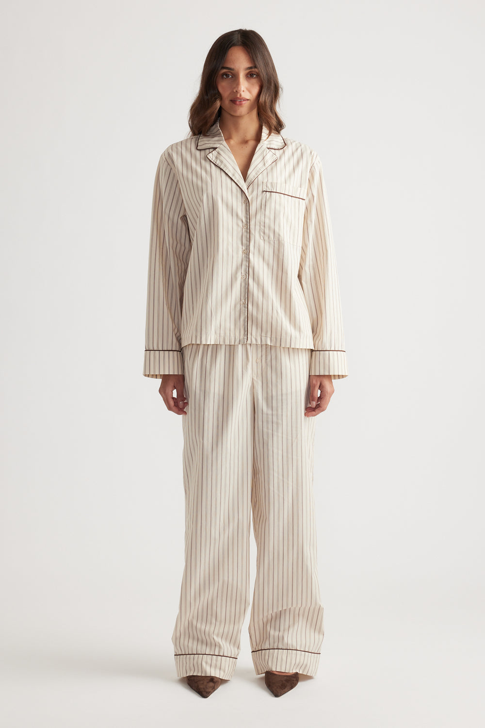 Woman wearing cream striped sleep woven long sleeve shirt and matching wide-leg pants with dark piping detail