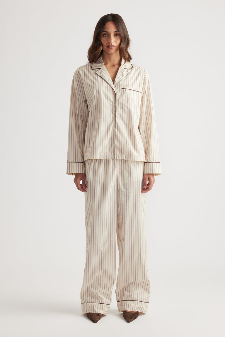 Woman wearing cream striped sleep woven long sleeve shirt and matching wide-leg pants with dark piping detail