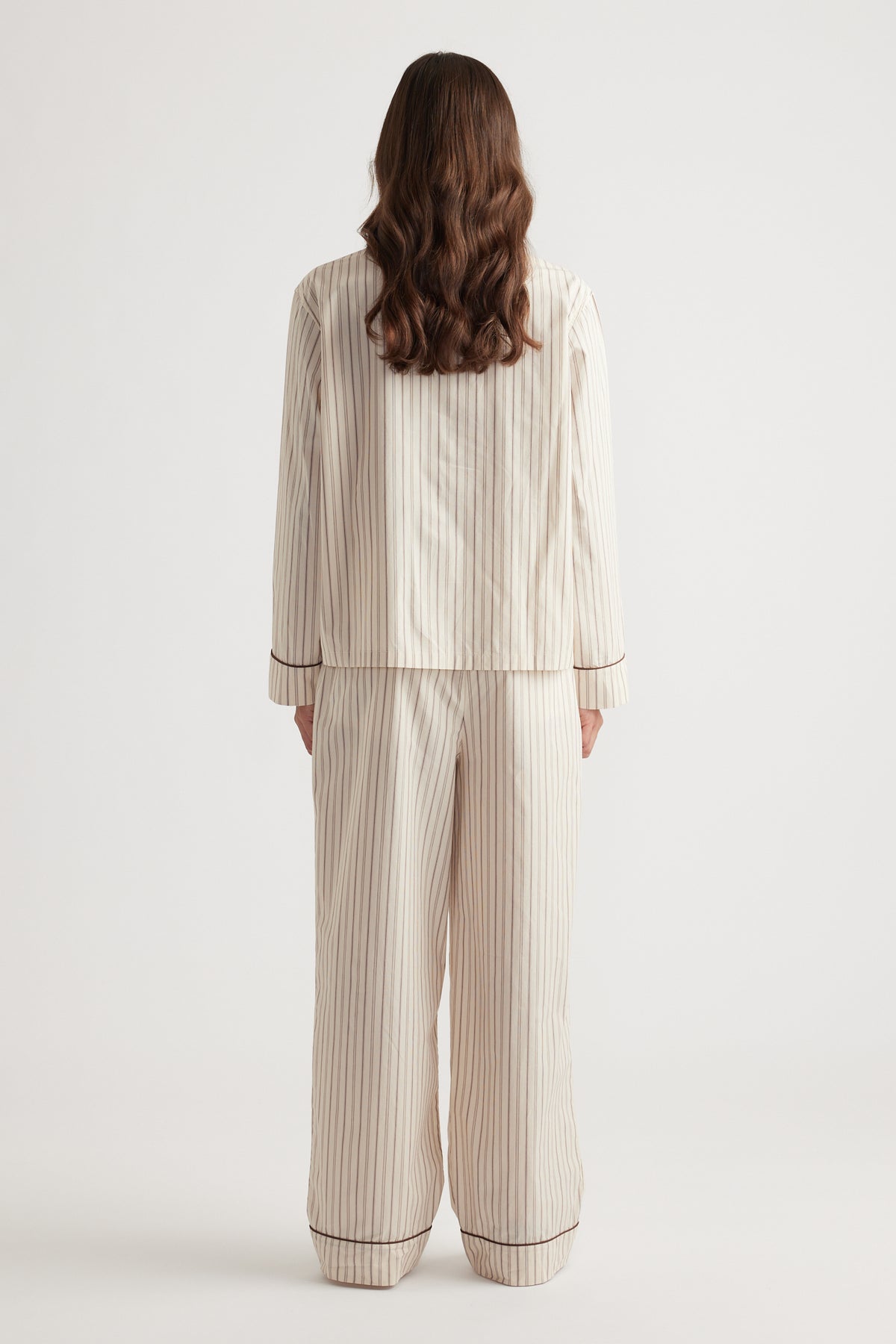 Woman wearing cream sleepwear set with vertical chocolate stripes and contrasting trim on cuffs and hems from the back