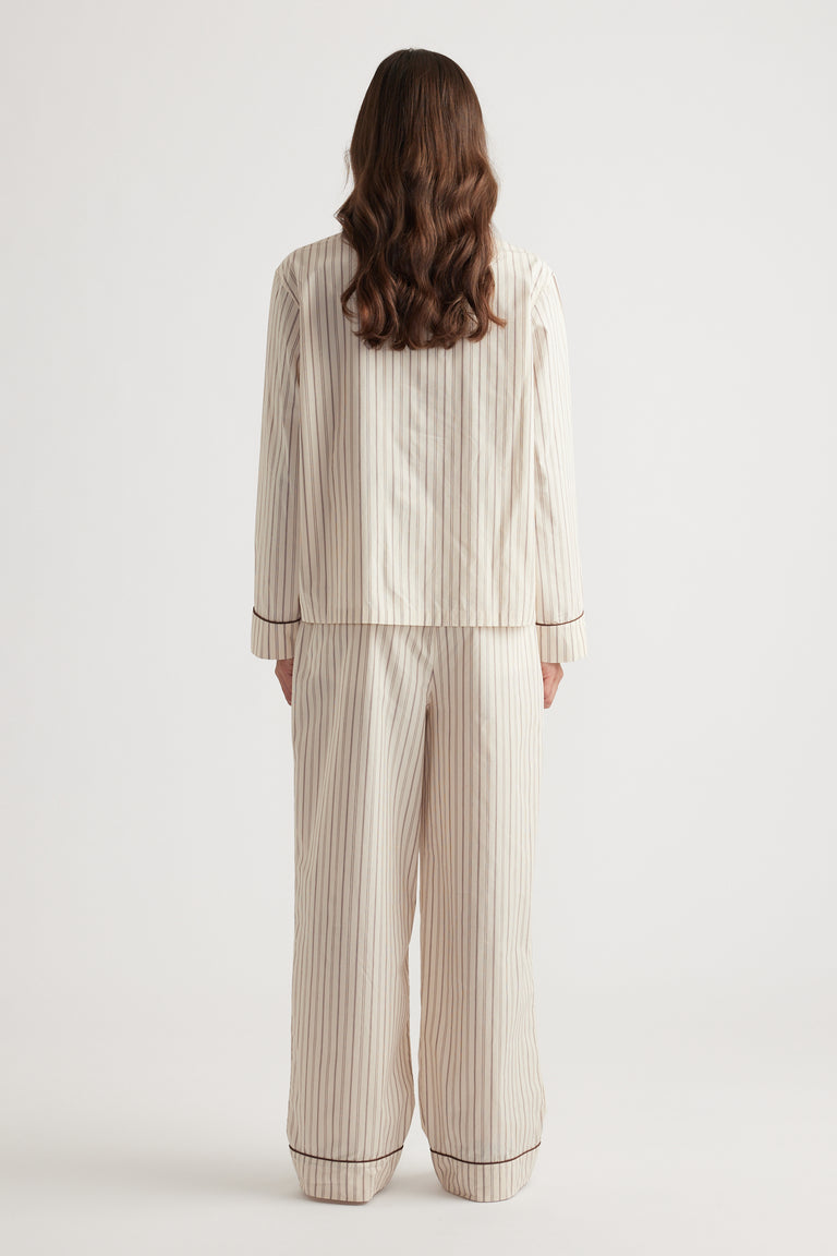 Woman wearing cream sleepwear set with vertical chocolate stripes and contrasting trim on cuffs and hems from the back