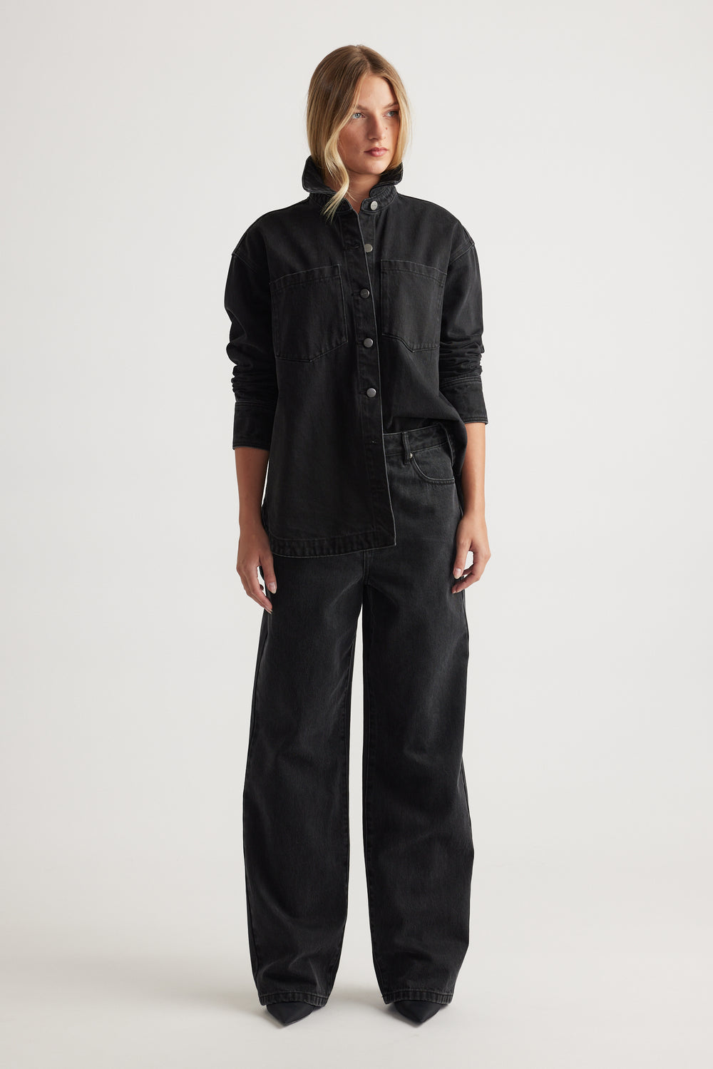 Woman wearing a black denim jacket and black wide leg jeans on a white background