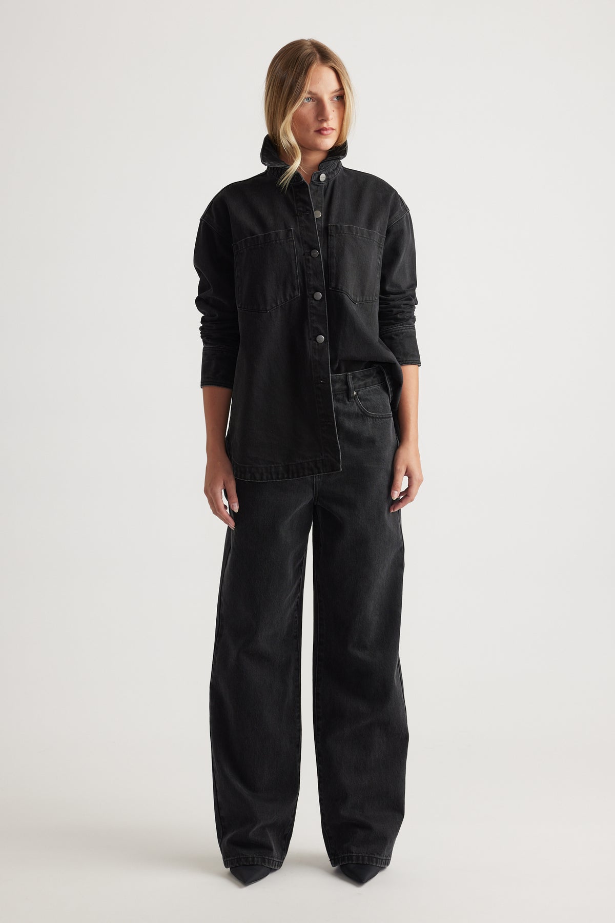 Woman wearing a black denim jacket and black wide leg jeans on a white background