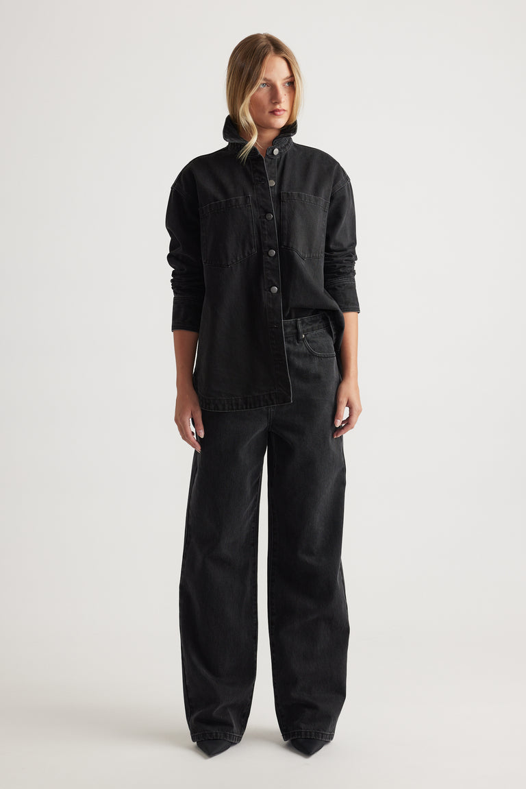 Woman wearing a black denim jacket and black wide leg jeans on a white background