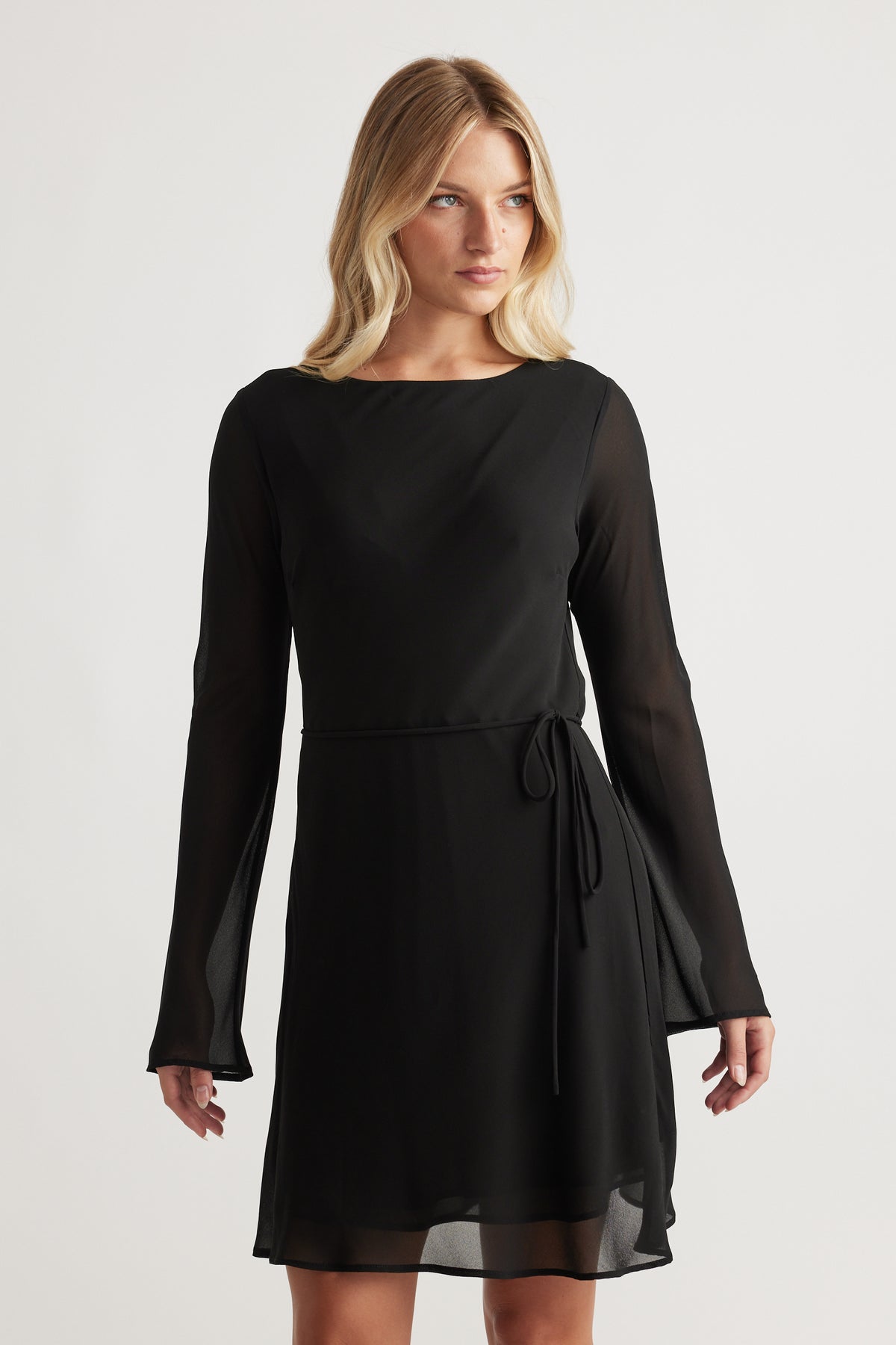 Woman wearing Chelsea Georgette Mini Dress in black with sheer long sleeves and a waist tie for a graceful look