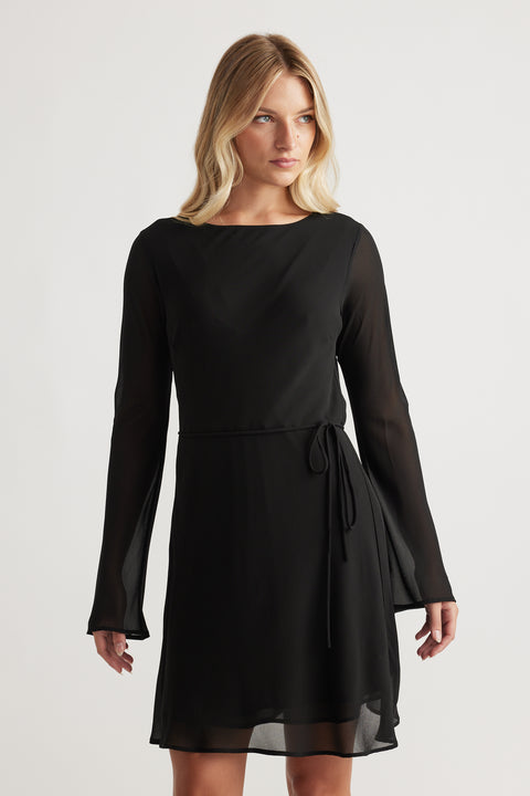 Woman wearing Chelsea Georgette Mini Dress in black with sheer long sleeves and a waist tie for a graceful look