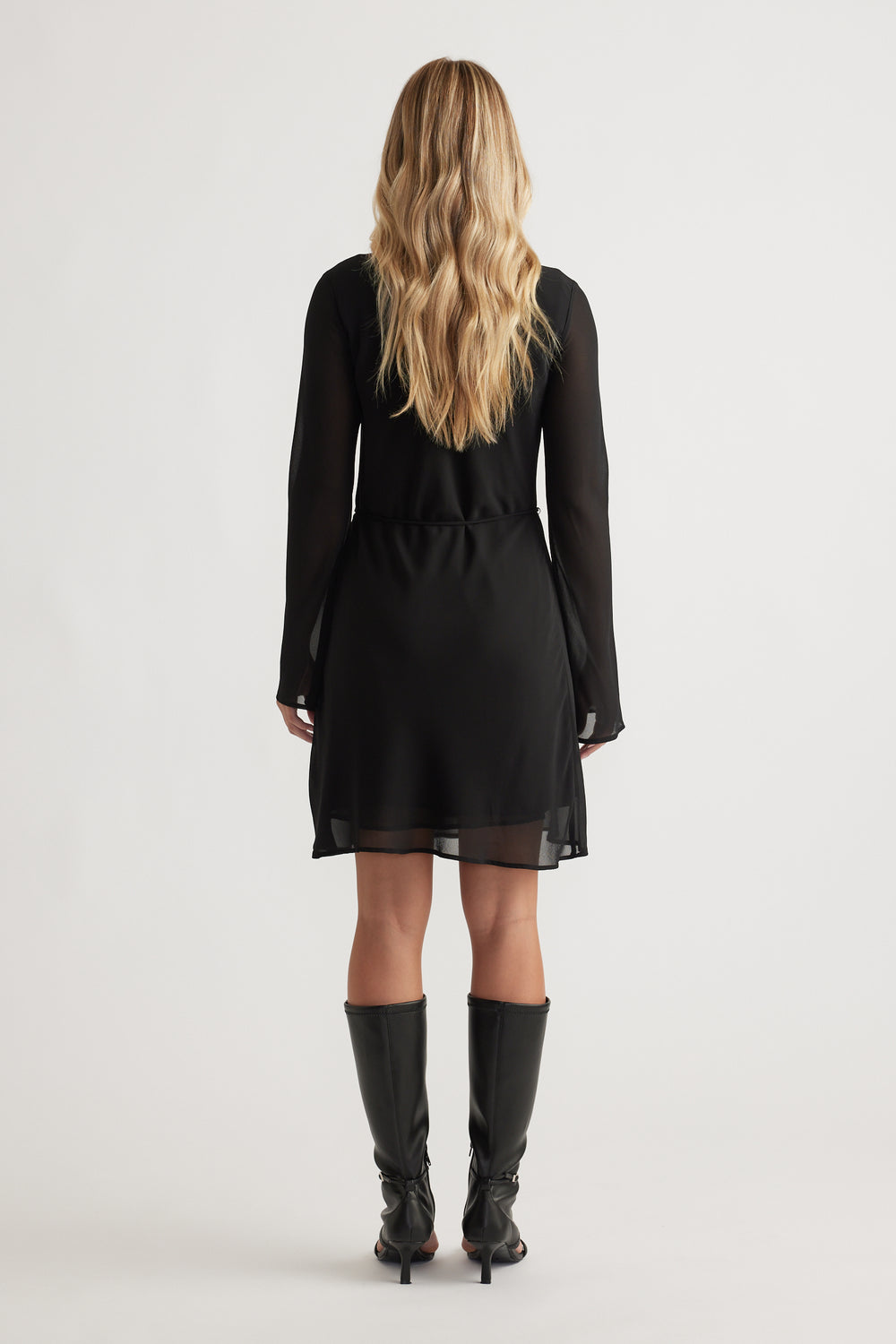 Back view of Chelsea Georgette Mini Dress in black with sheer long sleeves and layered hem, styled with knee-high boots