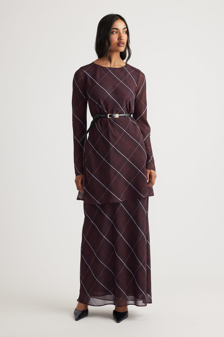 Woman wearing a long-sleeve layered maroon check-print dress with a slim black belt and black pointed shoes