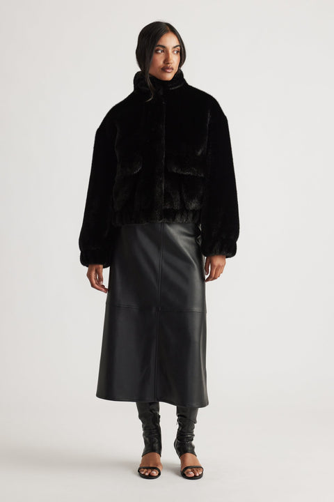 Woman wearing a black faux fur bomber jacket paired with a high-waisted faux leather midi skirt and open-toe heels