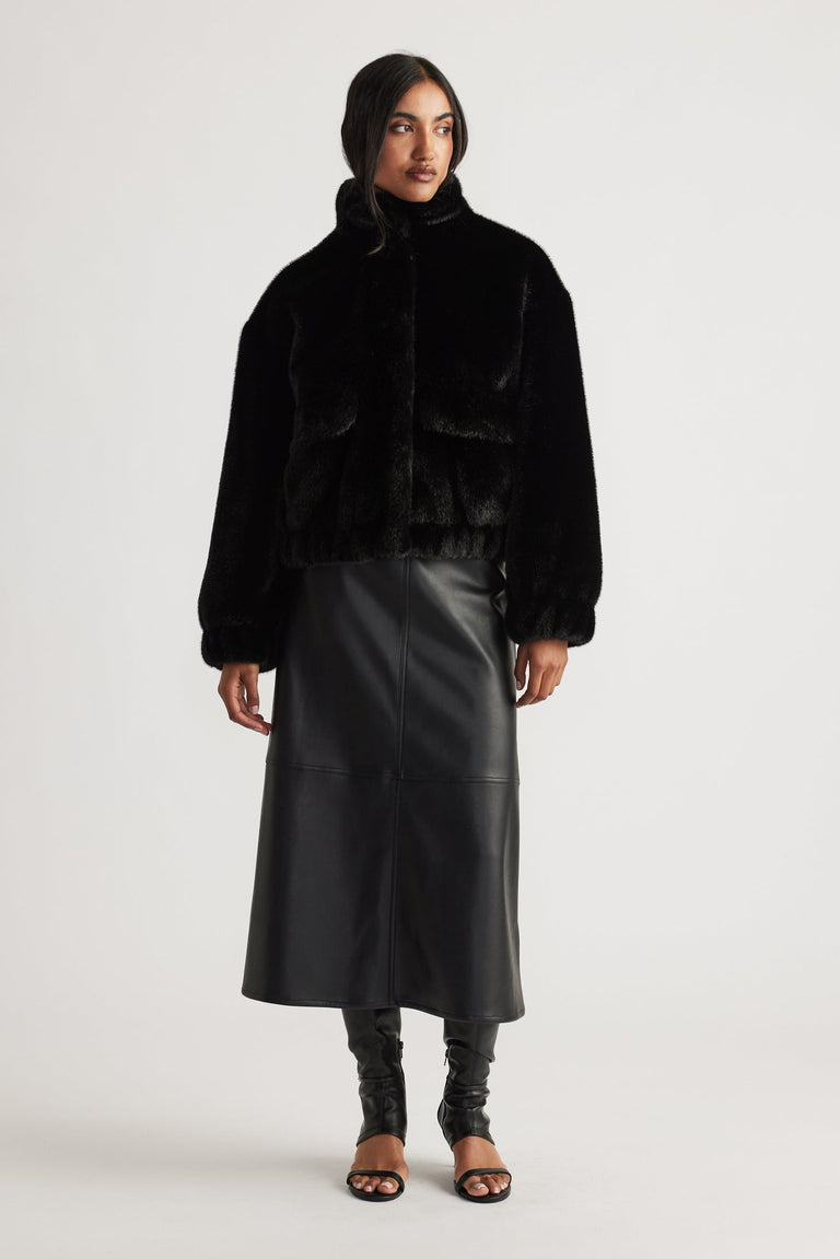 Woman wearing a black faux fur bomber jacket paired with a high-waisted faux leather midi skirt and open-toe heels