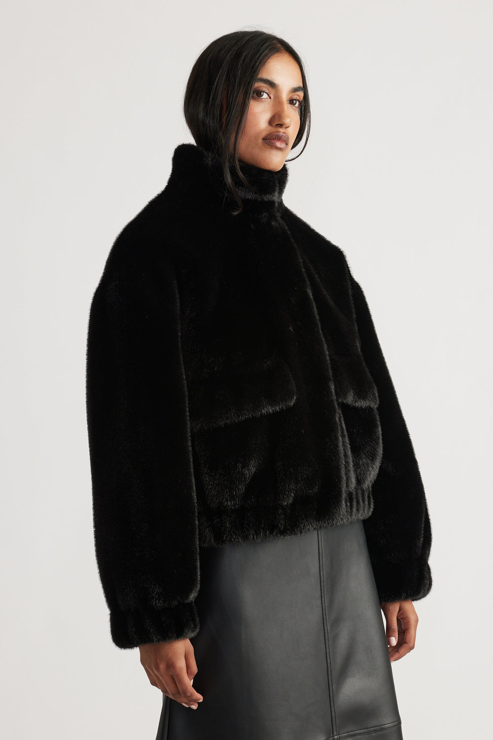 Woman wearing a black plush faux fur bomber jacket with a high collar paired with a sleek leather skirt