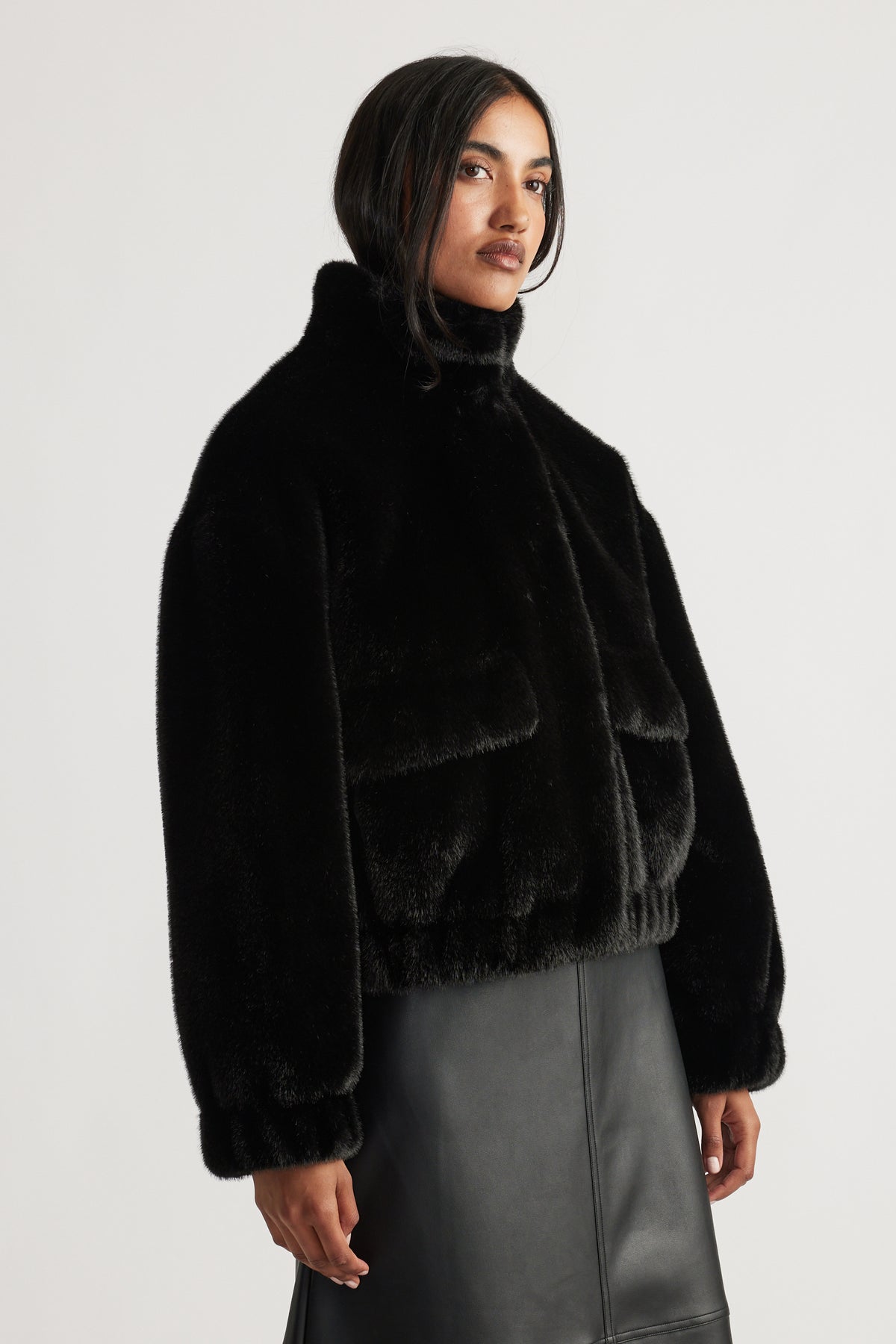 Woman wearing a black plush faux fur bomber jacket with a high collar paired with a sleek leather skirt