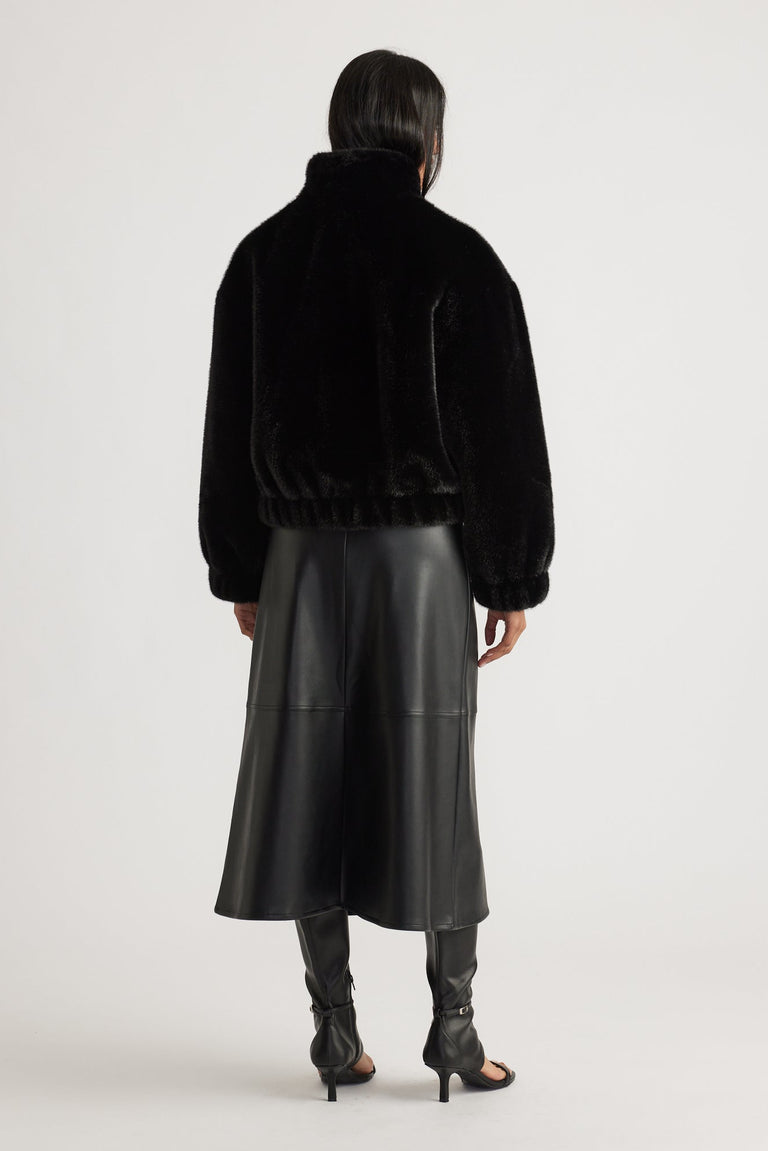 Woman wearing a black faux fur bomber jacket with elastic hem, paired with a sleek black leather midi skirt and heels.