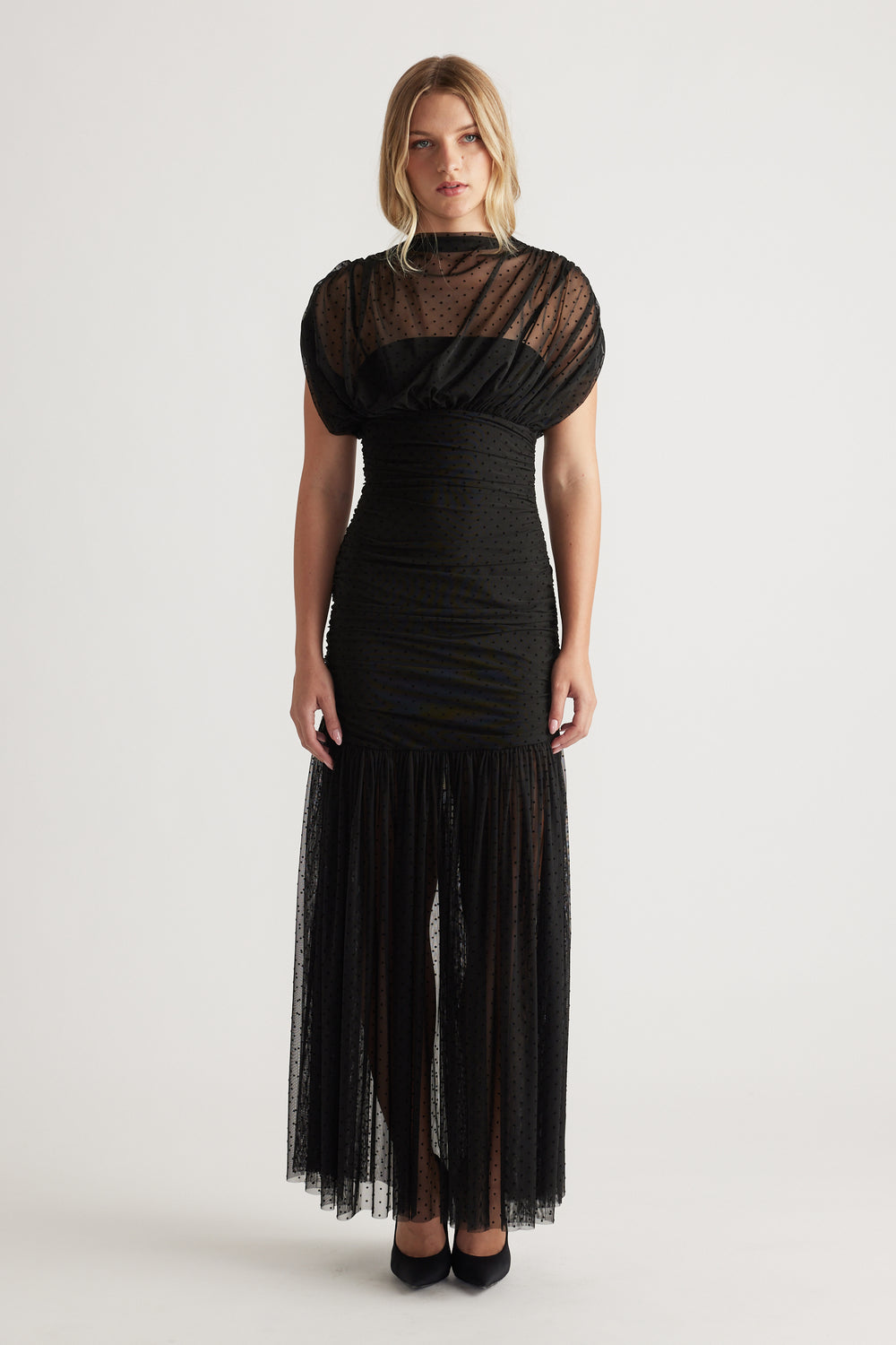 Front view of a woman wearing a black high neck mesh maxi dress with puffed sleeves and a sheer textured skirt panel