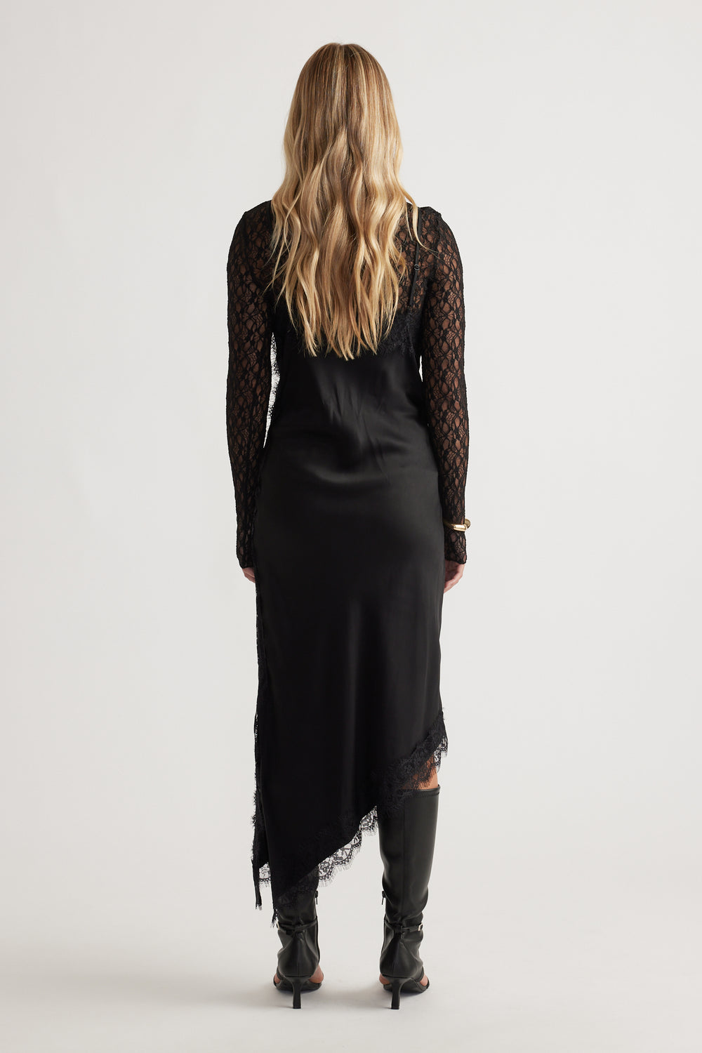 Back view of woman wearing Karla Lace Midi Dress with intricate lace sleeves and asymmetrical hem paired with black boots