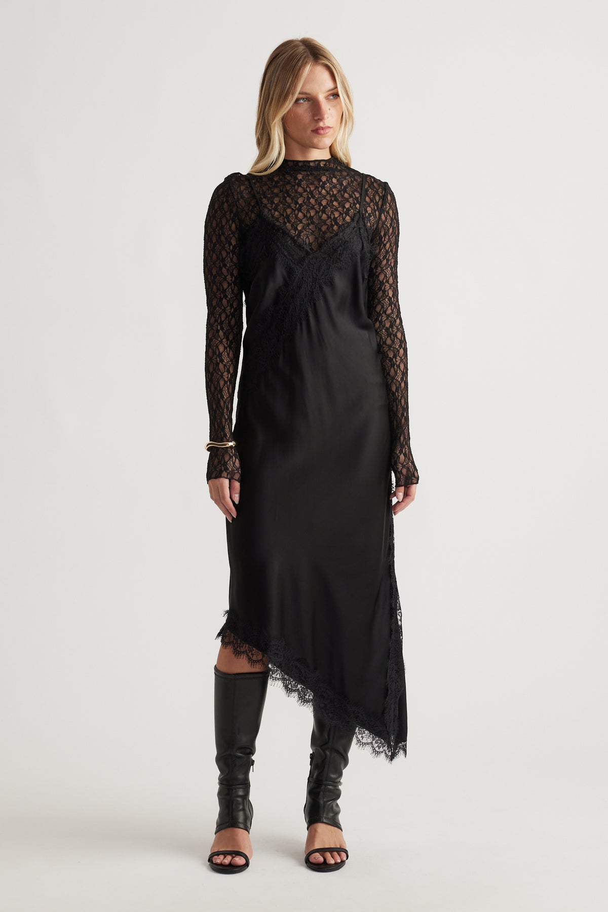 Woman wearing Karla Lace Midi Dress in black with asymmetrical hem styled with open-toe black boots by DECJUBA