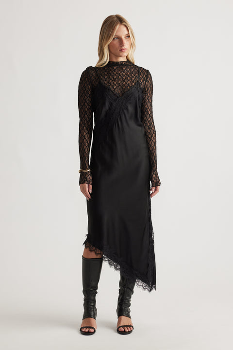 Woman wearing Karla Lace Midi Dress in black with asymmetrical hem styled with open-toe black boots by DECJUBA