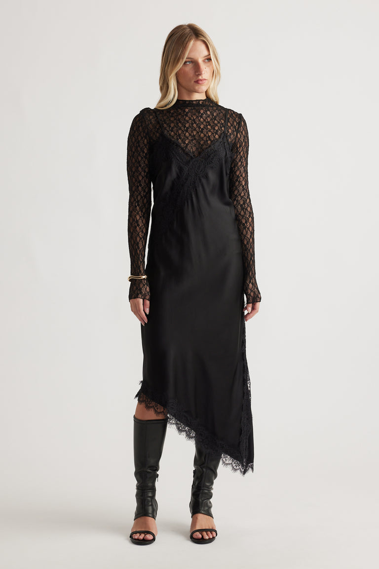 Woman wearing Karla Lace Midi Dress in black with asymmetrical hem styled with open-toe black boots by DECJUBA