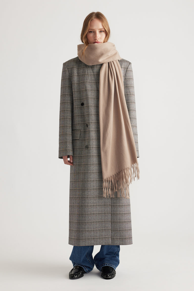 Woman wearing a long plaid coat layered with a soft biscuit-colored Gemma Solid Scarf featuring delicate fringe ends by DECJUBA