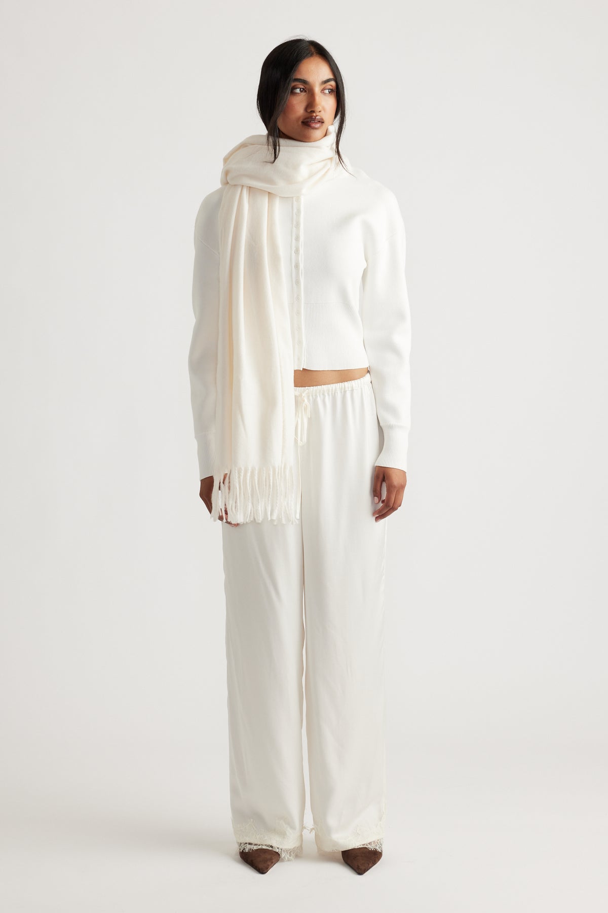 Woman dressed in an elegant all-white outfit featuring a soft, fringed cream scarf for a refined, cozy look