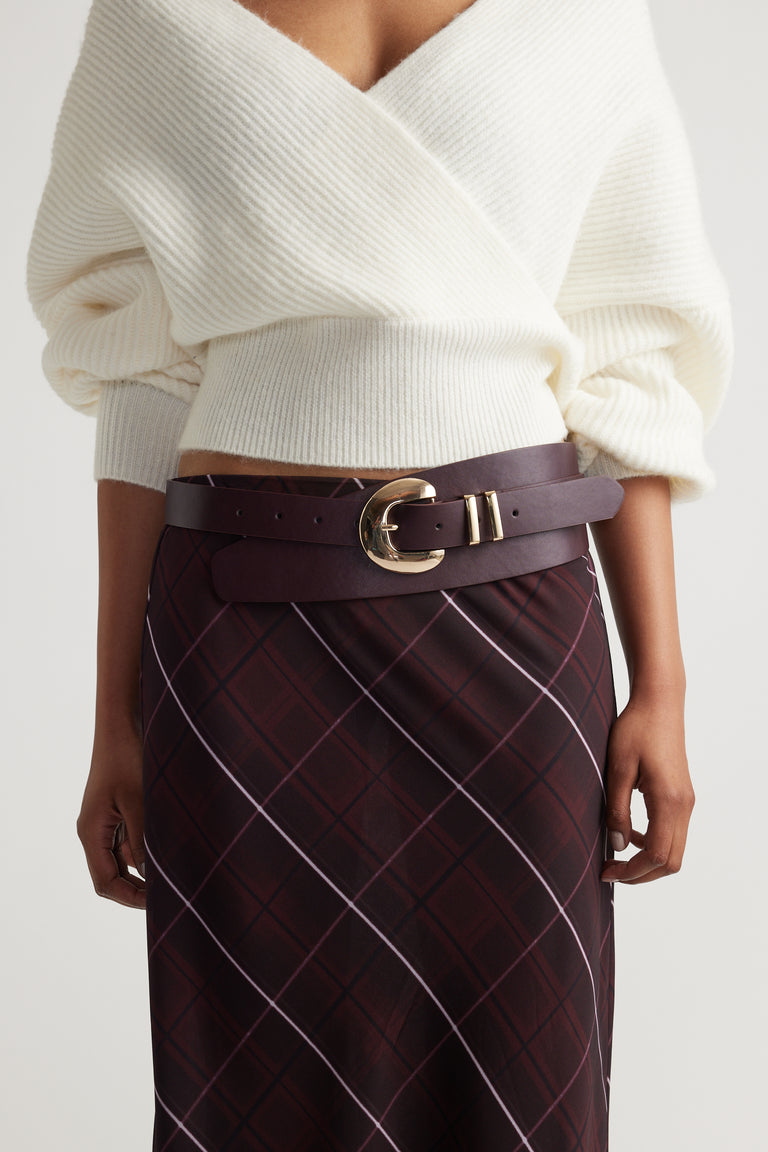 Vicci Wrap Belt in rich burgundy leather with a bold gold buckle, styled over a patterned skirt for a chic look.