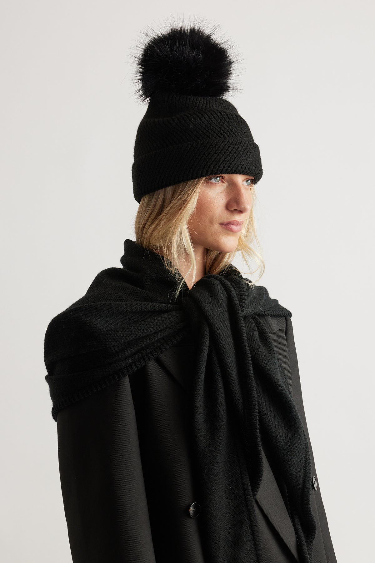 Woman wearing black Demi Pom Beanie with a fluffy pom paired with a matching black scarf and coat by DECJUBA.