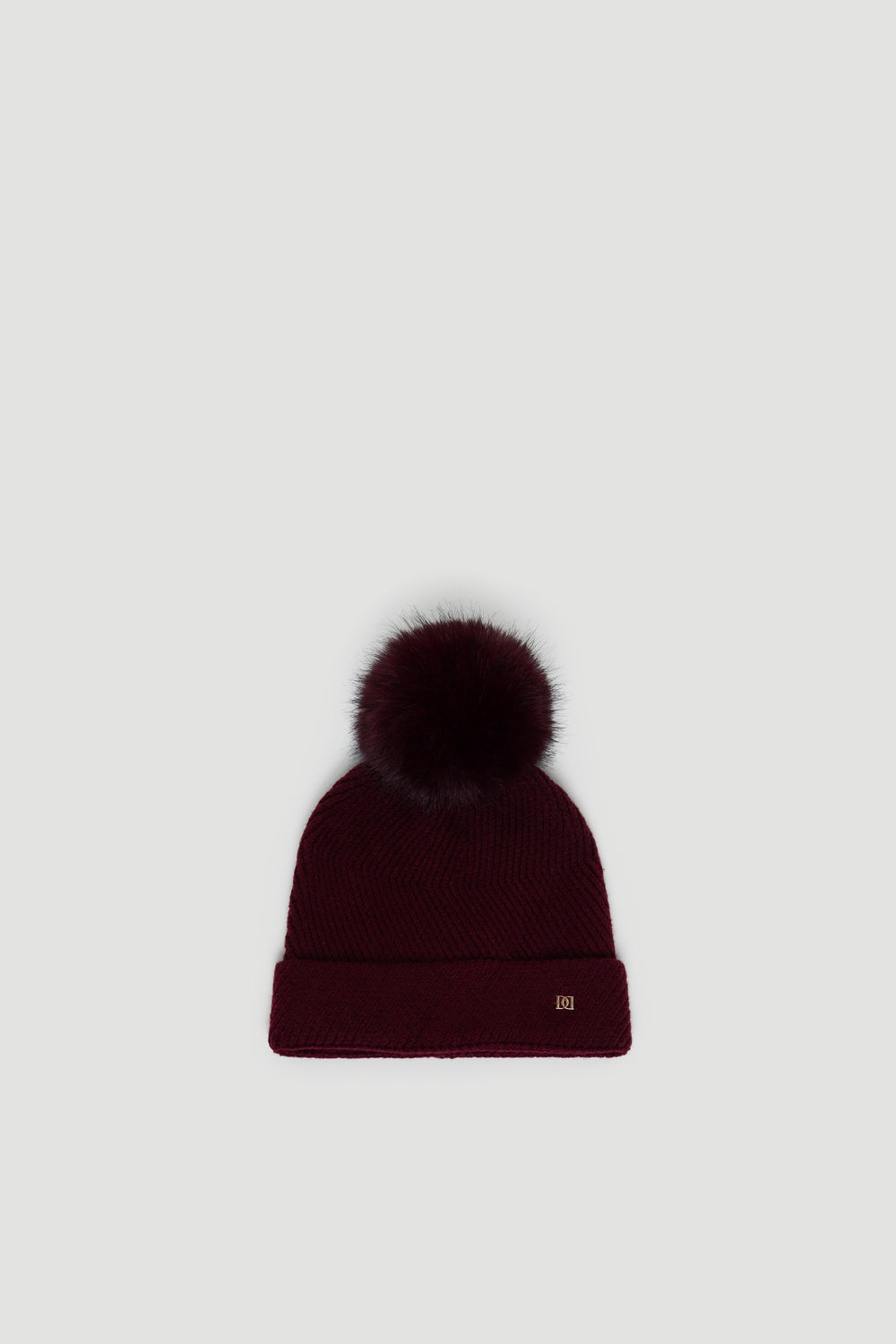 Plum-colored knit beanie with a fluffy pom-pom and a small gold-tone detail on the cuff edge.