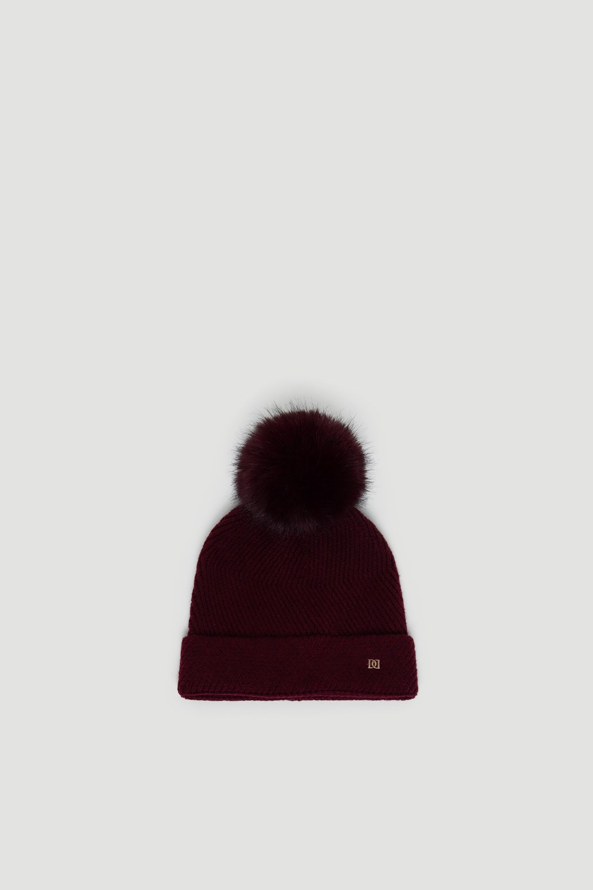 Plum-colored knit beanie with a fluffy pom-pom and a small gold-tone detail on the cuff edge.