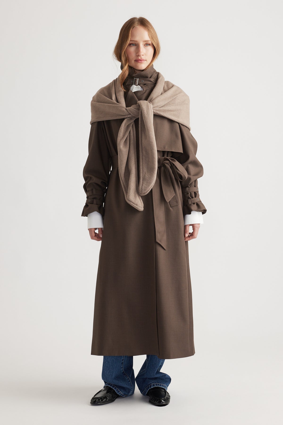 Woman styling Gracie Triangle Scarf in soft biscuit tone layered over a belted chocolate brown long coat with jeans and loafers