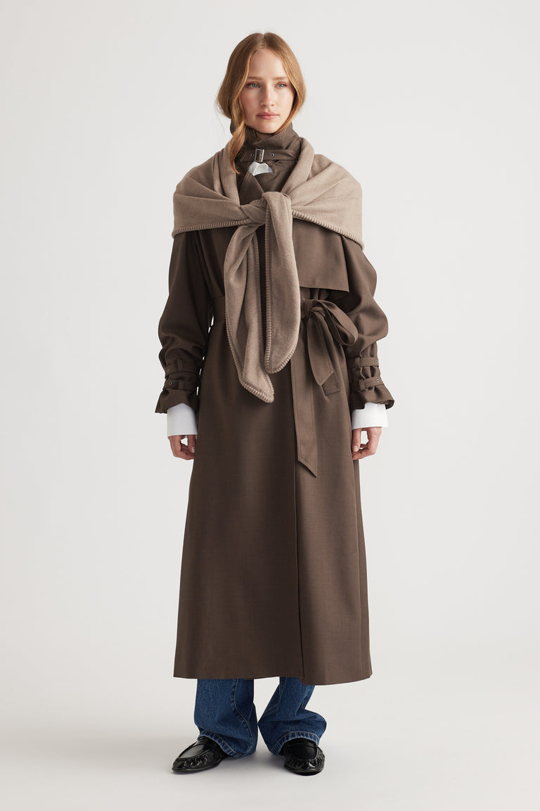 Woman styling Gracie Triangle Scarf in soft biscuit tone layered over a belted chocolate brown long coat with jeans and loafers