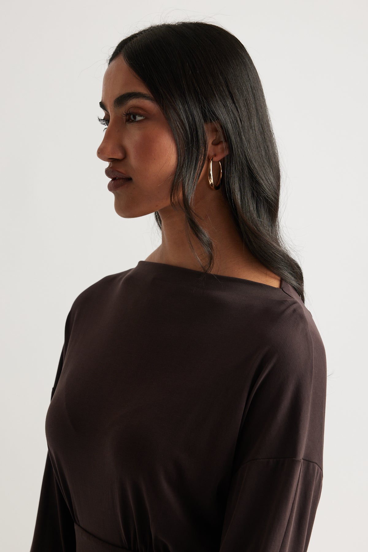 Side profile of a woman wearing gold Ellie Classic Hoop Earrings paired with a dark, elegant top by DECJUBA.
