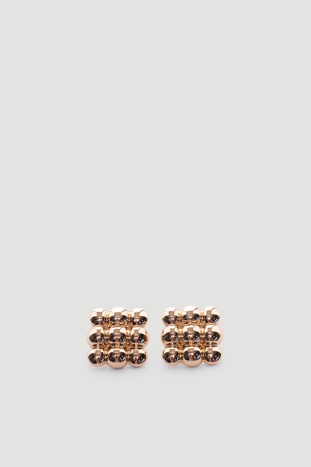 Pair of polished gold tone stud earrings featuring a modern grid of rounded square shapes with a reflective finish
