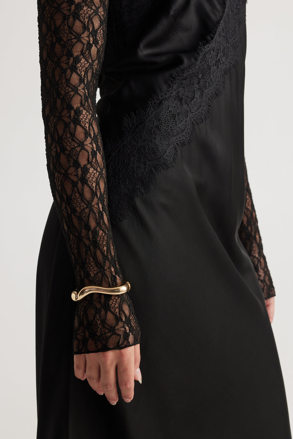 Ella Wavy Bracelet in polished gold tone with a sleek, curved design worn over a delicate black lace sleeve by DECJUBA.