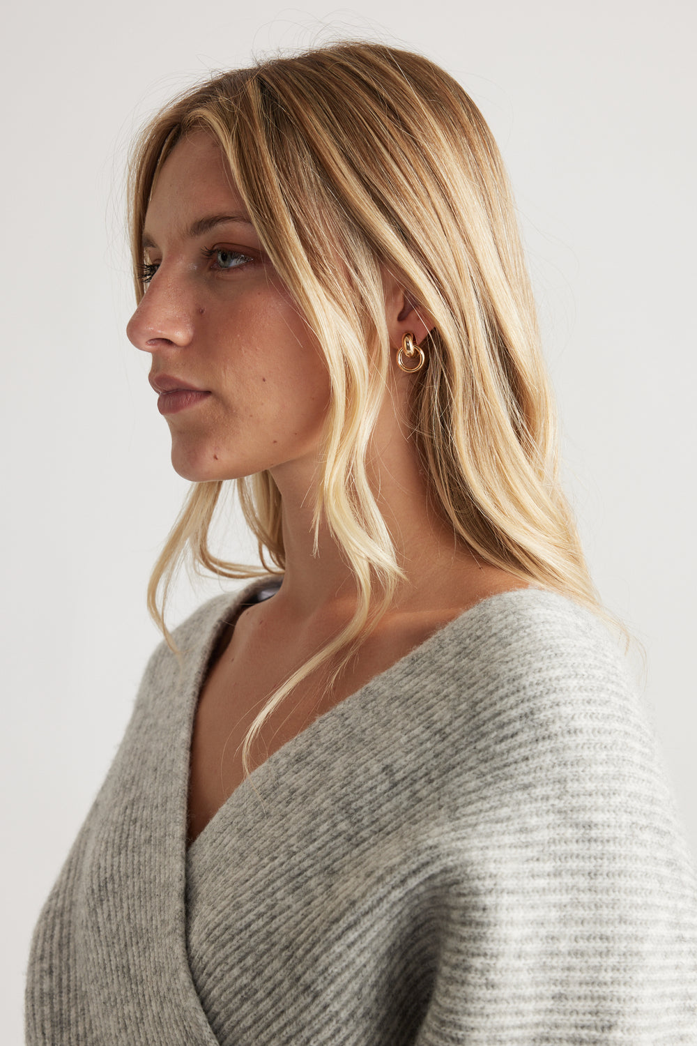 Profile view of woman wearing gold-tone Eden Earring Multi Pack styled with soft grey knitwear for a refined, everyday look.