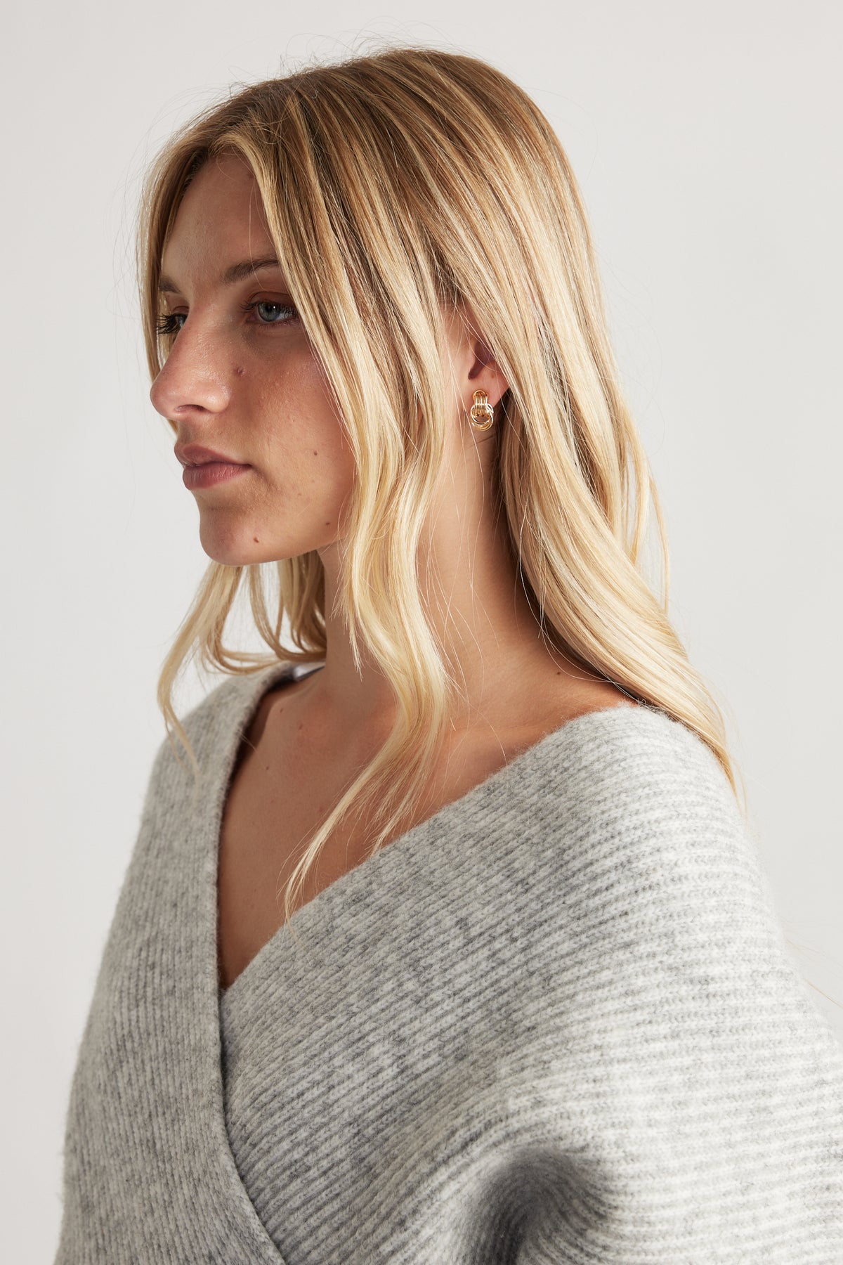 Close-up of woman wearing gold-tone Eden Earring Multi Pack styled with soft grey knitwear for a subtle, elegant look.
