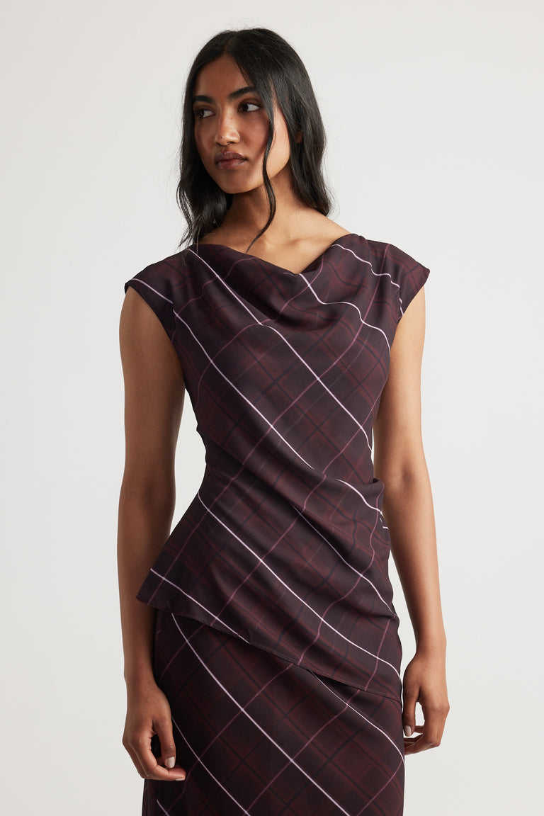 Woman wearing a sleeveless dark plaid top with a draped neckline and matching skirt against a plain backdrop